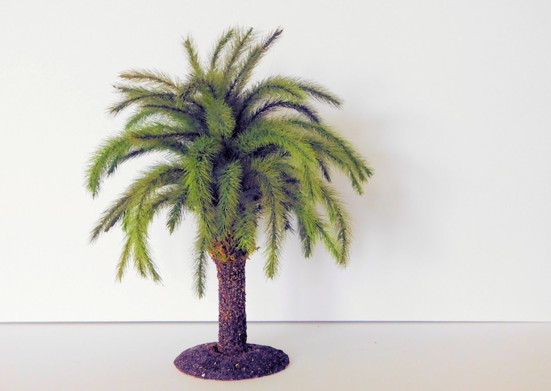 May include: A small, green artificial palm tree with a brown trunk and a base made of brown material.
