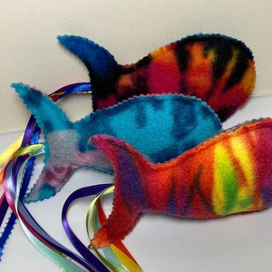 May include: Three colorful fish-shaped cat toys with long, multi-colored ribbons attached. The fish are made of soft, fuzzy fabric and have tie-dye patterns in shades of blue, pink, orange, and yellow.