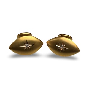 Könnte beinhalten: Ein Paar goldene Manschettenknöpfe, jeder mit einem einzelnen Diamanten, der in einem Sternmuster eingefasst ist.