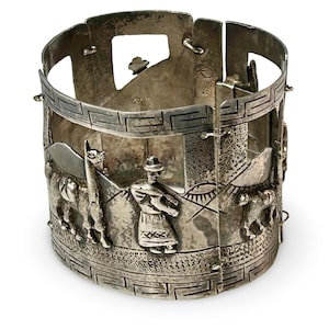 May include: A silver cuff bracelet with a detailed relief design. The bracelet features a repeating geometric pattern and scenes of people, llamas, and mountains. The clasp is visible on the side.