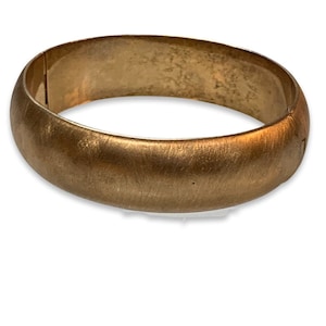 May include: A gold-toned bangle bracelet with a smooth, brushed finish.