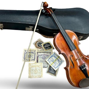 May include: A vintage violin with a bow and a black case. The violin has a warm, brown finish and black strings. Several Pirastro string packets are also visible.