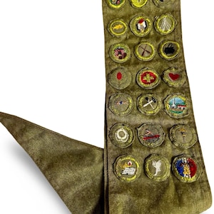May include: Olive green sash with multiple embroidered patches. The patches feature various designs, including a cross, a heart, and a lighthouse. The sash is made of a durable fabric and has a triangular end.