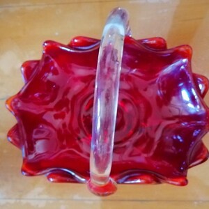 May include: A red glass bowl with a clear glass handle. The bowl has a scalloped edge and is shaped like a flower.