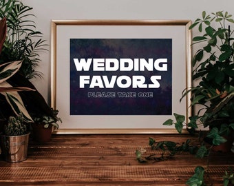 May include: A framed sign with gold trim displays the words "WEDDING FAVORS" in bold white letters against a dark blue and purple background. Below, the text reads "PLEASE TAKE ONE". The sign is on a wooden surface.