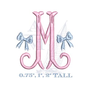 May include: A pink embroidered letter "M" with two light blue bows on either side. The letter has a decorative, cursive design. Text at the bottom reads "0.75", 1", 2" TALL".