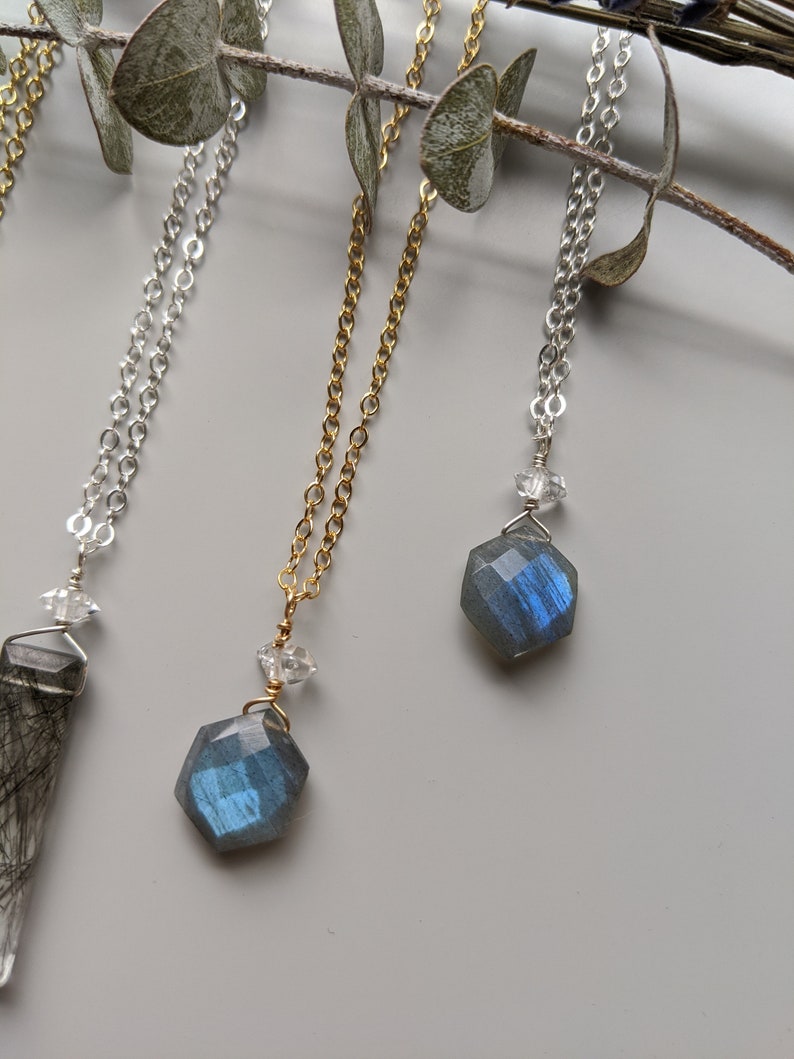 May include: Three necklaces with different chain styles and gemstone pendants. The pendants are all hexagonal and feature a blue labradorite stone. The chains are silver, gold, and silver.