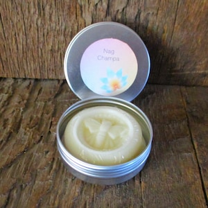 Peut inclure: Boîte ronde en métal argenté contenant un produit solide blanc cassé. Le couvercle porte l'inscription "Nag Champa" et un motif floral. Le produit est enveloppé dans du plastique transparent.