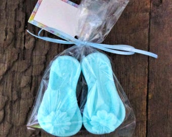 May include: Two light blue flip flop shaped soaps in a clear plastic bag tied with a blue ribbon. The soaps have a floral design.