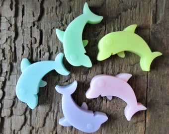 May include: Five pastel-colored dolphin shaped soap bars. The dolphins are in shades of light blue, green, yellow, pink, and purple.