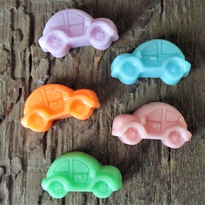 May include: Five colorful toy car charms in shades of purple, teal, orange, pink, and green are arranged on a rustic wooden surface. Each car has a rounded body and four circular wheels, perfect for crafting or embellishments.