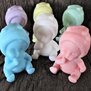 May include: Six small baby-shaped soaps in various pastel colors, including blue, pink, white, yellow, and purple. Each soap is shaped like a baby with a hooded hat and a finger in its mouth.