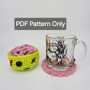May include: A crocheted brain-shaped bowl with a red and black stitched face and a pink crocheted coaster with a glass mug with a Halloween tree design. The mug reads "PDF Pattern Only".