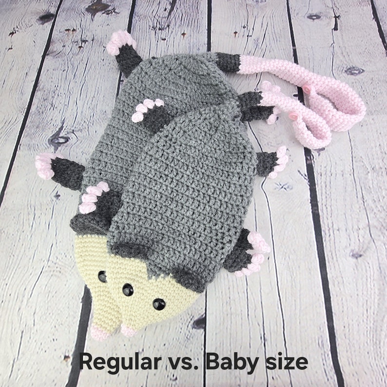 May include: Two crocheted opossum plushies, one larger than the other, with gray bodies, pink ears and tails, and yellow faces with black eyes. The text "Regular vs. Baby size" is below the plushies.