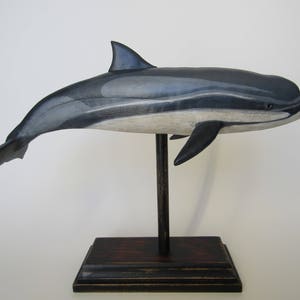 May include: A hand-carved wooden dolphin sculpture painted in shades of gray and white, mounted on a dark wood base.
