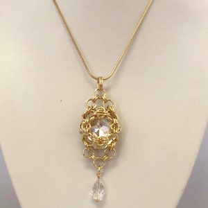 Puede incluir: Un collar de cadena de oro con un colgante que presenta un gran cristal transparente rodeado por un diseño de alambre dorado. Un cristal transparente más pequeño cuelga de la parte inferior del colgante.