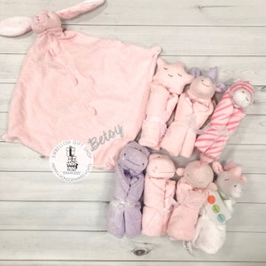 以下が含まれることがあります： ウサギ、星、カバ、キリンなど、さまざまな動物のキャラクターが描かれたピンクとパープルのベビーブランケットのセット。ブランケットには「Betsy」という名前と「Embellish Gift Shop」というテキストがパーソナライズされています。
