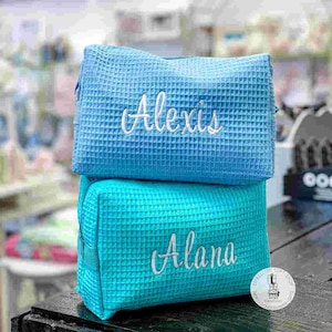 May include: Two blue waffle-textured zippered pouches with white embroidered names. The top pouch says "Alexis" and the bottom pouch says "Alana".