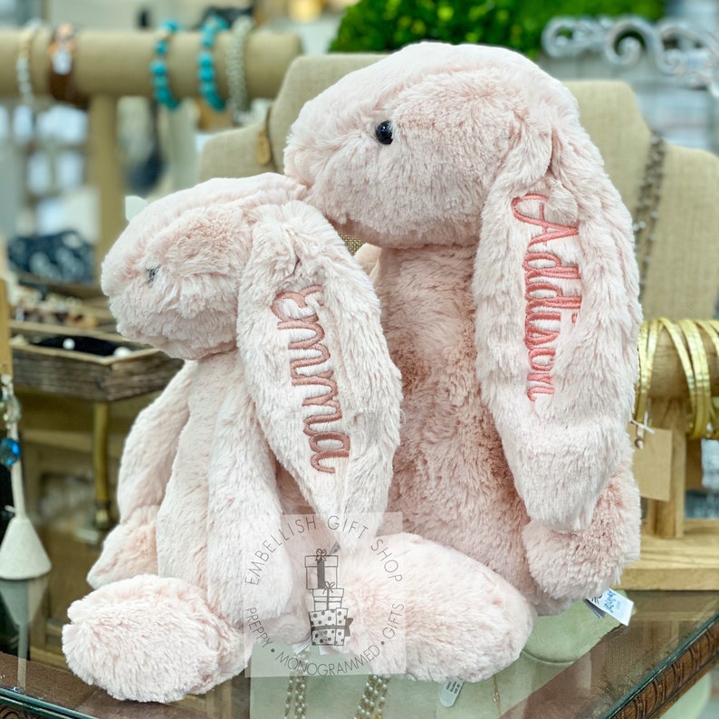 May include: Two pink plush bunny rabbits with embroidered names, "Emma" and "Addalyn", on their ears. The bunnies are sitting on a glass surface.