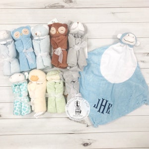 以下が含まれることがあります： フクロウ、サル、アヒルなど、さまざまな動物のデザインが施されたベビーブランケット10枚セット。ブランケットは、ブルー、ブラウン、グリーン、イエローです。ブランケットはリボンで結ばれており、タグには「Embellish Gift Shop」と「Preppy Monogrammed Gifts」の文字が書かれています。ブランケットは明るい木製の表面に並べてあります。