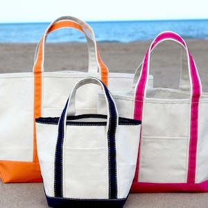 May include: Three canvas tote bags in different sizes. The largest bag has orange trim, the medium bag has navy blue trim, and the smallest bag has pink trim.