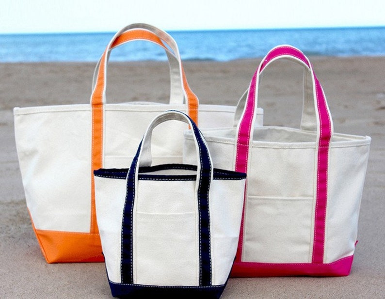 May include: Three canvas tote bags in different sizes. The largest bag has orange trim, the medium bag has navy blue trim, and the smallest bag has pink trim.