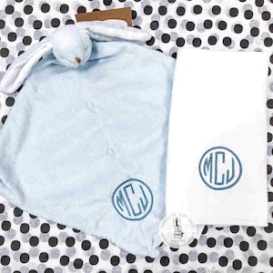 May include: A light blue baby blanket with a bunny attached. The blanket has a monogram of the letters "MCJ" in a circle. A white towel with the same monogram is also pictured.