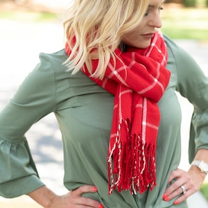 May include: A woman wearing a green blouse tied at the waist with a red and white plaid scarf. The scarf has white fringe.