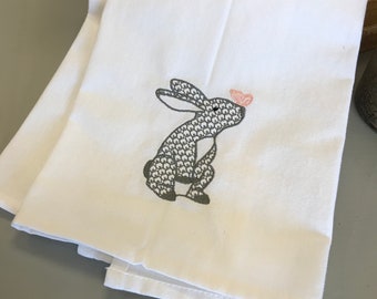 May include: A white kitchen towel with an embroidered gray bunny looking at a pink butterfly.