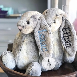 May include: Two gray plush bunny rabbits with long ears, one embroidered with the name "Ethan" and the other with the name "Isaac".