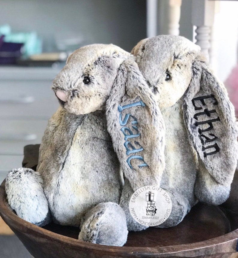 May include: Two gray plush bunny rabbits with long ears, one embroidered with the name "Ethan" and the other with the name "Isaac".
