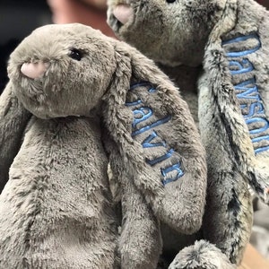 May include: Two gray plush bunny rabbits with blue embroidered names, "Olivia" and "Callie", on their ears.