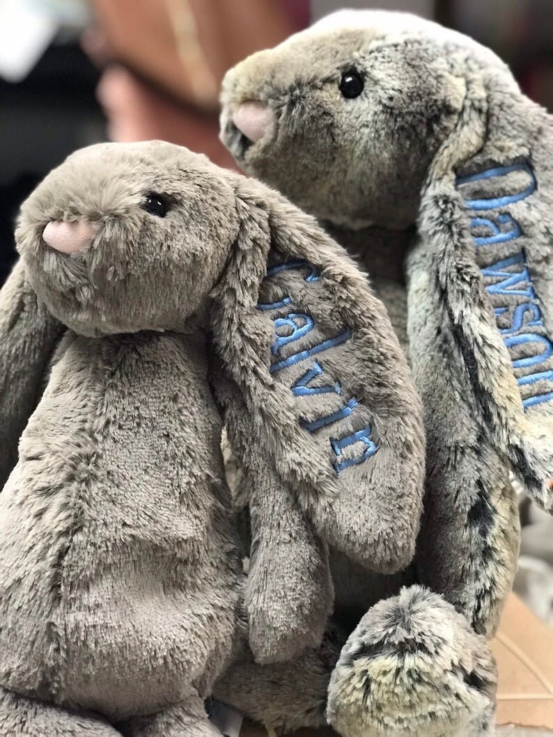 May include: Two gray plush bunny rabbits with blue embroidered names, "Olivia" and "Callie", on their ears.