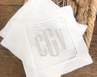 May include: Two white linen napkins with a scalloped edge and a monogram of the letters "CGV" embroidered in the center.
