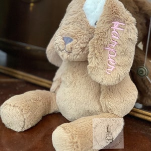 May include: A light brown plush dog toy with a white patch on its head. The dog has pink embroidered ears and the name "Harper" is embroidered on one ear.