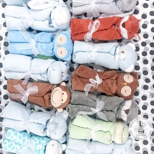 May include: A collection of 12 baby blankets, each featuring a different animal design. The blankets are made of soft, plush fabric and are tied with a white ribbon. The blankets are arranged in two rows of six, with the animals facing outwards. The blankets are all different colors, including blue, green, brown, and gray.