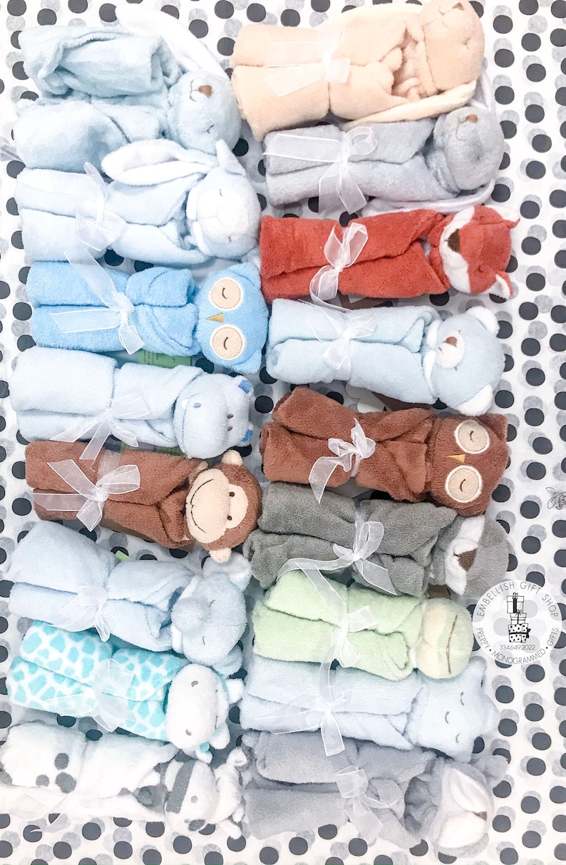 May include: A collection of 12 baby blankets, each featuring a different animal design. The blankets are made of soft, plush fabric and are tied with a white ribbon. The blankets are arranged in two rows of six, with the animals facing outwards. The blankets are all different colors, including blue, green, brown, and gray.
