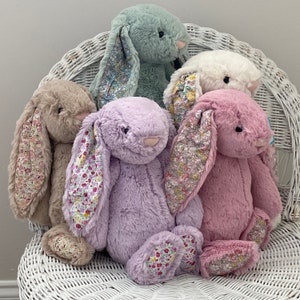 May include: Four plush bunny toys with floral patterned ears. The bunnies are in various colors, including light green, white, lavender, and pink.