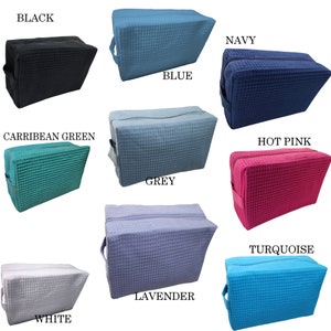 May include: A collection of rectangular cosmetic bags in various colors, including black, blue, navy, Caribbean green, grey, hot pink, white, lavender, and turquoise. Each bag features a waffle-weave texture, a zipper closure, and a handle.