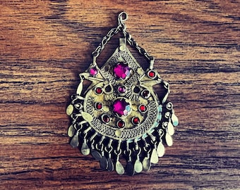 May include: A silver pendant with intricate details and pink gemstones. The pendant is teardrop shaped and is adorned with dangling charms.