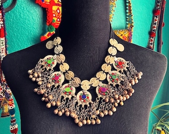 May include: A silver and gold necklace with colorful glass beads and dangling charms. The necklace is made of round metal discs and has a tribal or ethnic style.