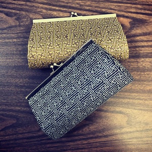 May include: Two small, decorative purses with a geometric pattern. The top purse is gold with a black pattern. The bottom purse is black with a silver pattern.