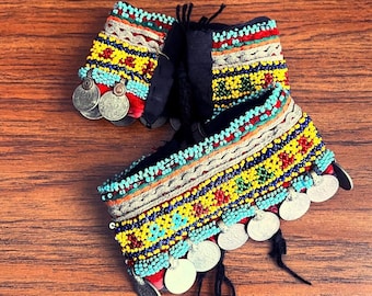 May include: Two colourful beaded bracelets with silver coin accents. The bracelets are made with a variety of beads in shades of blue, red, yellow, and green. The coins are attached to the bracelets with black thread.