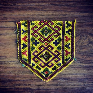 May include: A yellow, red, blue, and green beaded pattern with a geometric design. The pattern is sewn onto a fabric backing.