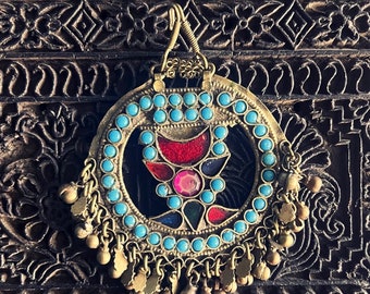 May include: A circular pendant with a blue and gold design. The pendant features a central motif of a multi-colored glass design surrounded by a ring of blue beads. The pendant is attached to a gold chain with a series of small bells.