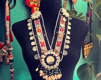 May include: A layered necklace with silver and white beads, a shell and mirror centerpiece, and colorful fabric accents.