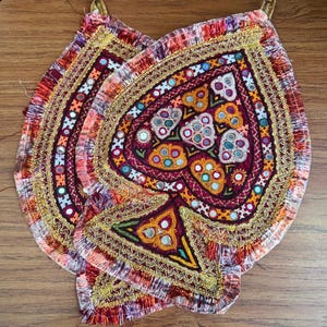 May include: Two heart-shaped fabric wall hangings featuring intricate embroidery in shades of red, orange, and yellow. The pieces are decorated with small circular mirrors, gold-colored metallic thread, and a fringe border along the edges.