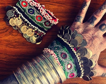 May include: Two bracelets with silver coins and colorful fabric. The bracelets are on a wooden surface and one is being worn on a hand.