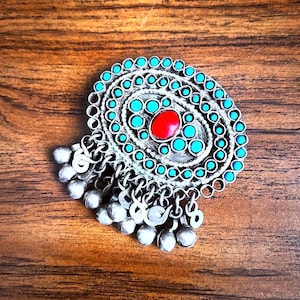 May include: A silver oval pendant with a turquoise and red stone design. The pendant has a fringe of silver beads.