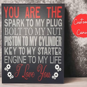 A black canvas sign with red and gray text that reads: "YOU ARE THE SPARK TO MY PLUG BOLT TO MY NUT PISTON TO MY CYLINDER KEY TO MY STARTER ENGINE TO MY LIFE I Love You," with small gear graphics.